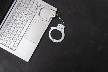 Handcuffs and laptop on dark background top view. Piracy, internet hacking and punishment for...
