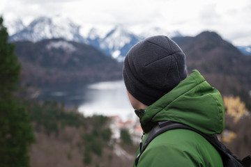 a male tourist in a green jacket with a backpack looks at the mountains