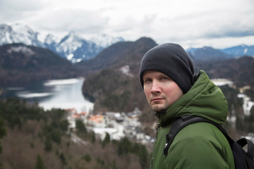 a male tourist in a green jacket with a backpack looks at the mountains