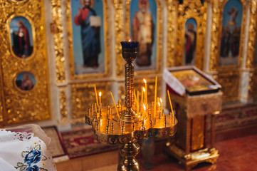 Yellow burning candles on a gilded counter stand in the church. Photography, concept.