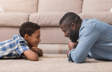 Afro father and son lying on carpet looking at each other