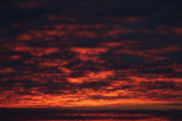 Crimson sky with clouds illuminated by the sun at sunset or sunrise at dusk