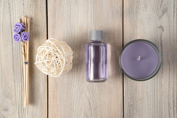 Spa composition of a bottle of oil, candles, wooden incense sticks with roses and a purple napkin on a wooden background.