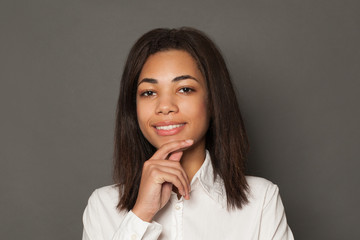 Smart young black woman student smiling on gray background, face close up