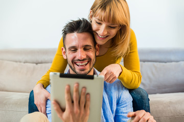 Young couple laughing at home in the living room using digital tablet. 