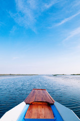 Thai wooden boat bow travel in peaceful blue Nong Harn lake - Udonthani, Thailand. Famous red lotus lake in winter
