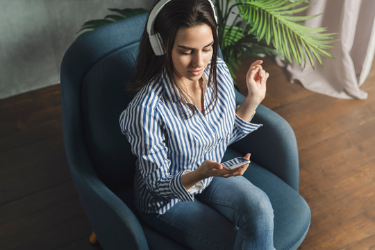 Woman listening to broadcast streaming it online on smartphone. Great entertainment content with music, videos and podcasts. Young woman relaxing, enjoying music, wearing headphones. Downloaded apps.