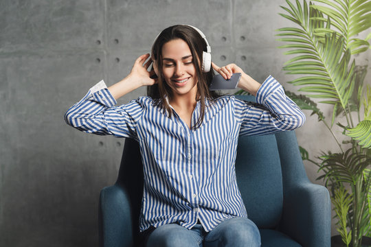 Happy millennial woman listening to broadcast streaming it online on smartphone. Great entertainment content with music, videos and podcasts. Young woman enjoying music, wearing headphones.