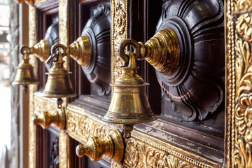 Fototapeta na wymiar Antique bronze bells on a wooden door with inlaid Hindu temple. Close-up
