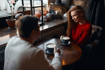 blonde awesome girl and handsome guy having a date indoors, young people warm themselves with hot yummy flat white.
