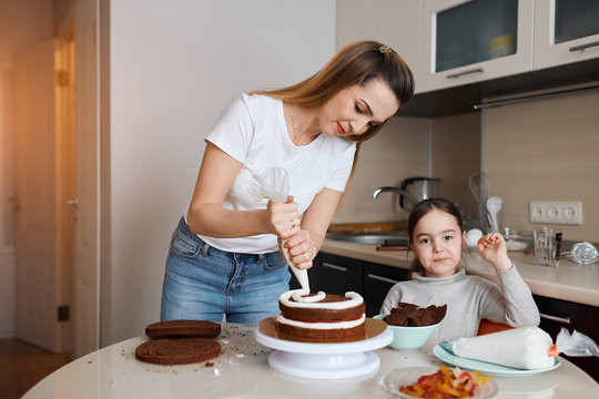 young woman in T-shirt an djeans concentrated on decorating dessert, while her child looking at the camera. close up photo