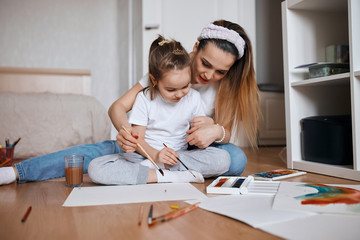 young woman and her daughter concentrated on painting process while sitting on the floor. close up photo