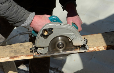 Joiner hands hold a circular saw cutting a board, close up