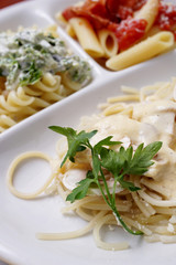 A white plate with three types of cooked  pasta