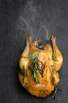 Roasted poussin with rosemary on black stone background