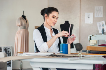 Shot of a Sunny Fashion Design Studio. We See Working Personal Computer, Hanging Clothes, Sewing Machine and Various Sewing Related Items on the Table, Mannequins Standing, Colorful Fabrics.