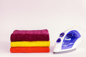 Bright warm knitted clothes stacked in a pile with a bright iron on a white background