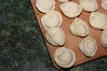 Dumplings on a wooden board on a green background. Top view on a green table with homemade food. Uncooked handmade dumplings on a wooden plate.