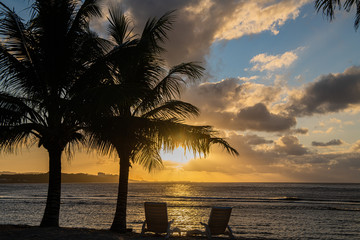 Romantic sunset with palm trees on the ocean with two sun loungers.
