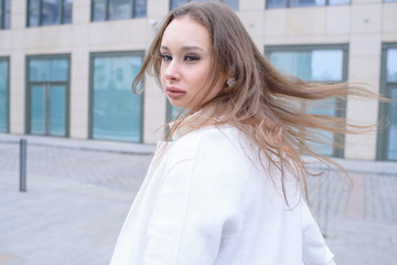 Young beautiful girl walking in a white coat in cloudy weather. Portrait photo session. Fashion.