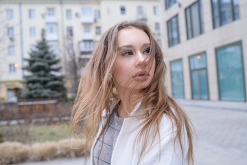 Fototapeta premium Young beautiful girl walking in a white coat in cloudy weather. Portrait photo session. Fashion.