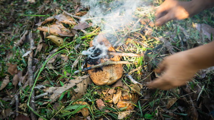 Making a fire using a hot coal from dried tree branches and coconut fiber on the ground.