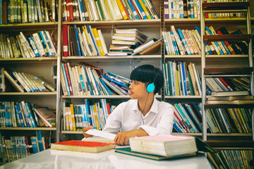 The abstract art design background of Young teenager wearing headphone on her head,reading and searching data from book,at library,blurry light around