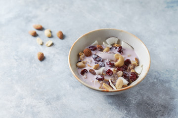 Bowl of granola with yogurt, nuts, cranberry and cocoanut on bright stone  background.