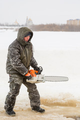 Naklejka premium Worker in a green jacket with a hood with a chainsaw in his hands