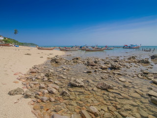 view of many small rocks on sand beach with many fishing boats floating in the sea and blue sky background, Klong Hin Beach, Ko Lanta island, Krabi, southern of Thailand.