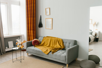 The interior of the living room in a Scandinavian minimalist style in gray-yellow-orange colors: sofa, coffee table, mirror