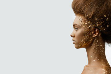 Fashion art portrait of model girl with holiday golden shiny professional makeup. woman with gold metallic body and hair on white background. Gold glowing skin. copy space