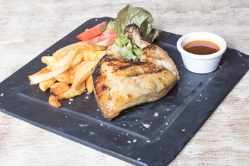 Chicken leg with potatoes, salad, tomato and sauce on black stone plate