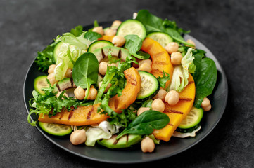 plate of pumpkin salad, avocado, cucumber, chickpeas, lettuce on a stone background.