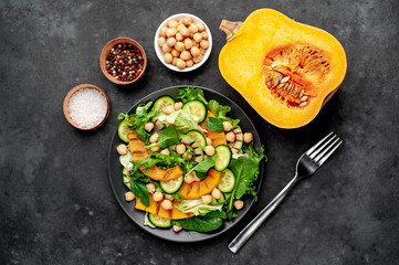 plate of pumpkin salad, avocado, cucumber, chickpeas, lettuce on a stone background.