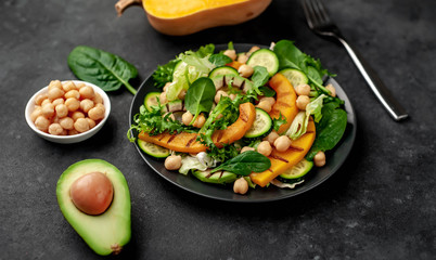 plate of pumpkin salad, avocado, cucumber, chickpeas, lettuce on a stone background.