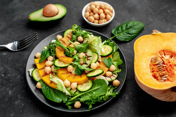 plate of pumpkin salad, avocado, cucumber, chickpeas, lettuce on a stone background.