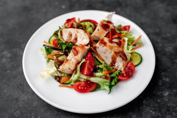 a plate of salad of tomato, chicken, cucumber, carrots, soy sauce in a plate on a stone background