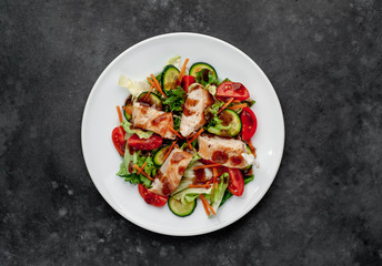 a plate of salad of tomato, chicken, cucumber, carrots, soy sauce in a plate on a stone background