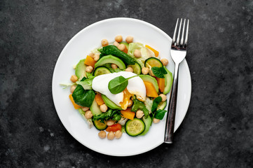 a plate of avocado salad, chickpeas, pumpkin, cucumber, poached egg in a plate on a stone background