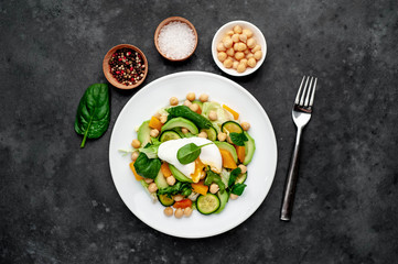 a plate of avocado salad, chickpeas, pumpkin, cucumber, poached egg in a plate on a stone background