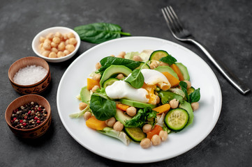 a plate of avocado salad, chickpeas, pumpkin, cucumber, poached egg in a plate on a stone background
