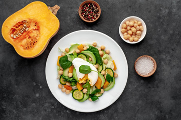 a plate of avocado salad, chickpeas, pumpkin, cucumber, poached egg in a plate on a stone background