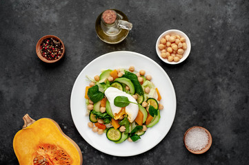 a plate of avocado salad, chickpeas, pumpkin, cucumber, poached egg in a plate on a stone background