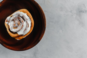 cinnamon bun with white chocolate on a wooden plate and a dark background