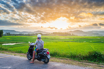 Obraz na płótnie Canvas One person on motorbike looking at view of rice fields and mountains in the Phu Yen province, Nha Trang Quy Nhon, adventure traveling in Vietnam. Rear view sunburst backlight dramatic sky at sunset.