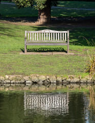 Bench on the grass at Chiswick House and Gardens, reflected in the water.  Chiswick, London UK