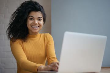 Beautiful African American business woman using laptop computer, sitting in office. Portrait of...