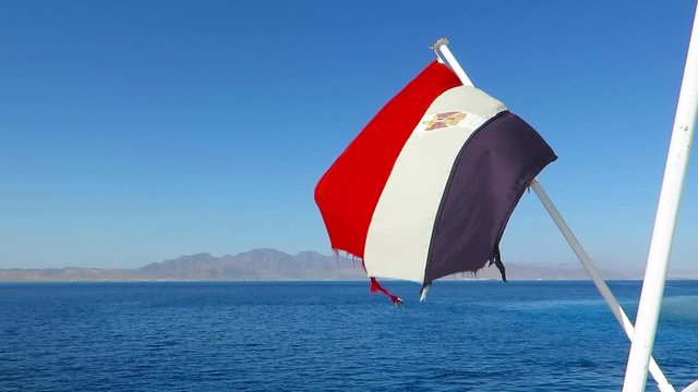 Egyptian flag in the wind above the Red sea. Flagpole on the ship with moving banner. Red sea adventure ship with Egyptian flag.