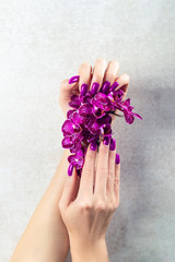 Stylish trendy purple female manicure. Woman hands are holding orchid flowers